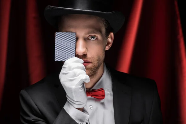 Professional magician showing trick with playing card in circus with red curtains — Stock Photo