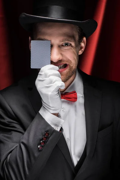Mago emotivo mostrando trucco con carta da gioco in circo con tende rosse — Foto stock
