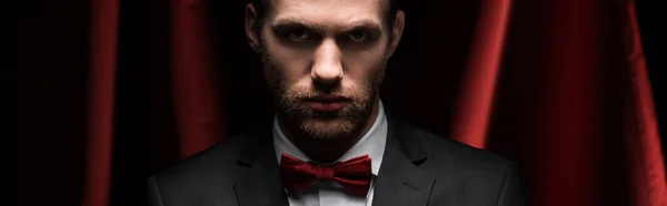 Panoramic shot of concentrated man in suit and bow tie in circus with red curtains — Stock Photo