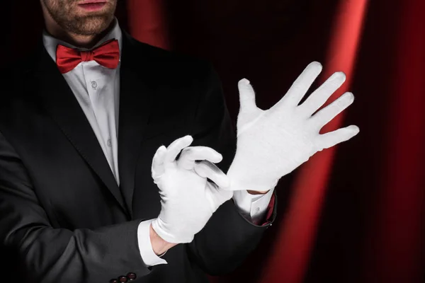 Cropped view of magician wearing gloves in circus with red curtains — Stock Photo