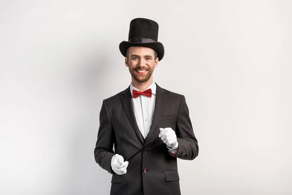 Feliz mago con traje y sombrero sosteniendo varita, en gris - foto de stock