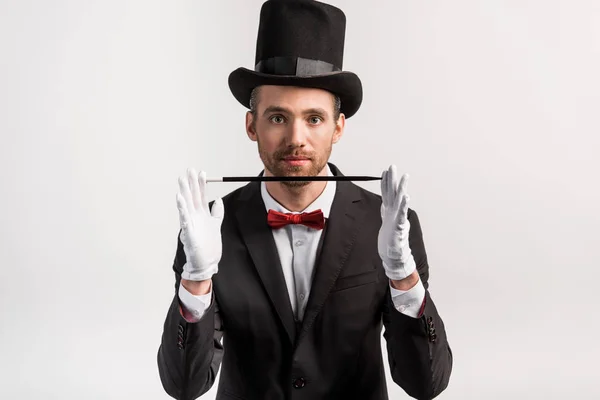 Молодой фокусник в костюме и шляпе с палочкой, изолированный на сером — стоковое фото