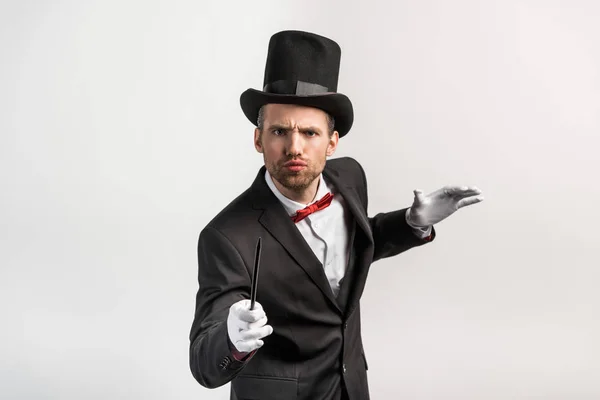 Magicien inquiet en costume et chapeau tenant baguette, isolé sur gris — Photo de stock
