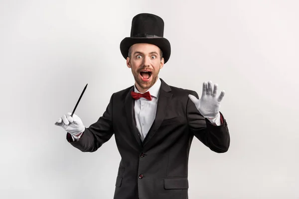 Excited magician in suit and hat holding wand, isolated on grey — Stock Photo