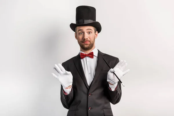 Magicien adulte avec geste haussant les épaules tenant la baguette, sur gris — Photo de stock