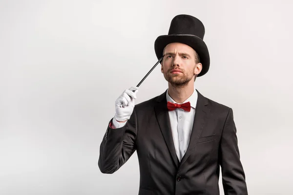 Pensive magician in suit and hat holding wand, isolated on grey — Stock Photo