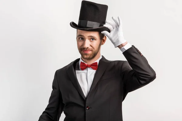 Handsome happy magician adjusting hat, isolated on grey — Stock Photo