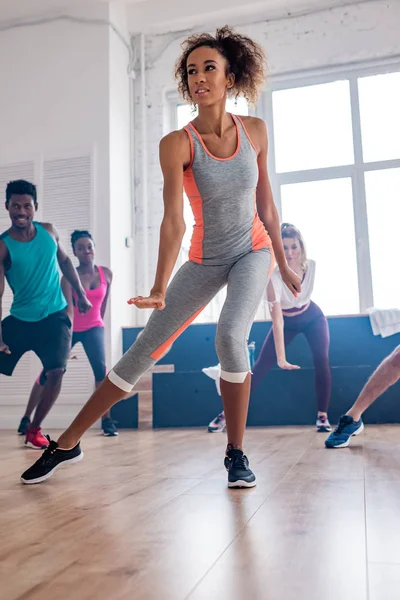 Low angle view of beautiful african american trainer practising with zumba dancers in studio — Stock Photo