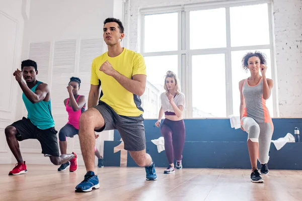 Low angle view of handsome trainer performing zumba with multiethnic dancers in dance studio — Stock Photo