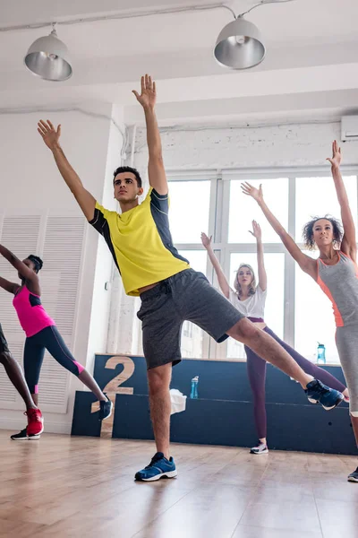 Vista de baixo ângulo de dançarinos multiétnicos com as mãos no ar praticando zumba no estúdio de dança — Fotografia de Stock