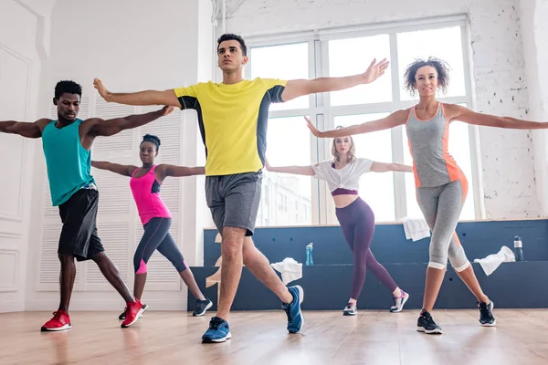 Vista de bajo ángulo del entrenador guapo realizando zumba con bailarines multiculturales en estudio - foto de stock