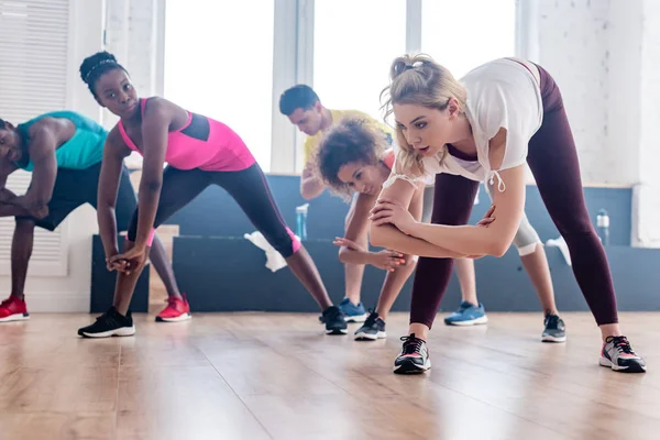 Vista de bajo ángulo del entrenador estirándose con bailarines multiétnicos de zumba en estudio - foto de stock