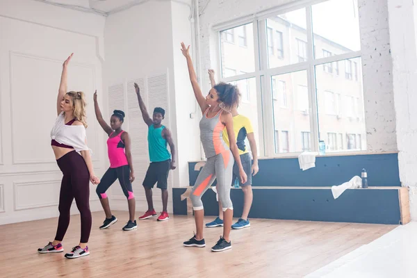 Entraîneur et danseurs multiethniques avec les mains en l'air pratiquant la zumba en studio de danse — Photo de stock