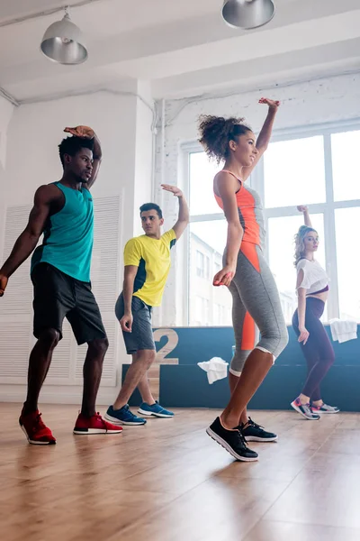 Vista lateral de jovens dançarinos multiculturais com as mãos no ar dançando zumba em estúdio — Fotografia de Stock