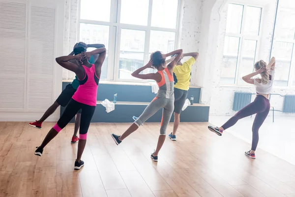 Vista posterior de bailarines multiétnicos realizando movimientos de zumba en estudio de danza - foto de stock
