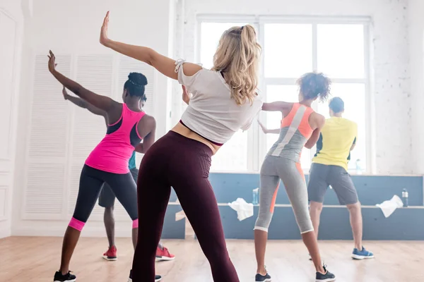 Vue arrière de danseurs de zumba multiethniques exécutant des mouvements dans un studio de danse — Photo de stock