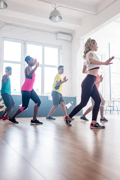 Vista lateral de bailarines multiculturales entrenando movimientos de zumba en estudio de danza - foto de stock