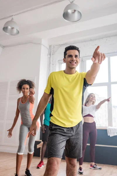 Enfoque selectivo de entrenadores y bailarines multiétnicos apuntando con el dedo mientras bailan zumba en estudio - foto de stock