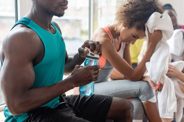 Focus selettivo della ballerina afroamericana che tiene una bottiglia sportiva mentre riposa in studio di danza — Foto stock