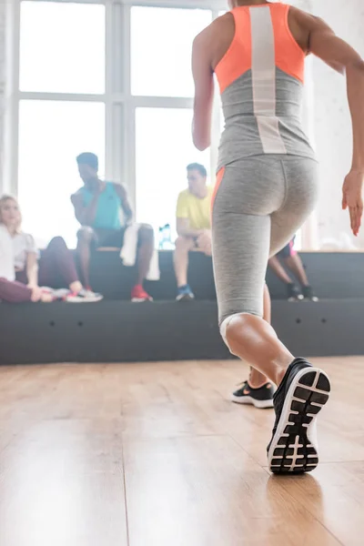 Selective focus of young woman stretching with multicultural zumba dancers at background in dance studio — Stock Photo