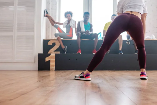 Selective focus of young girl stretching with multiethnic zumba dancers on bench in dance studio — Stock Photo