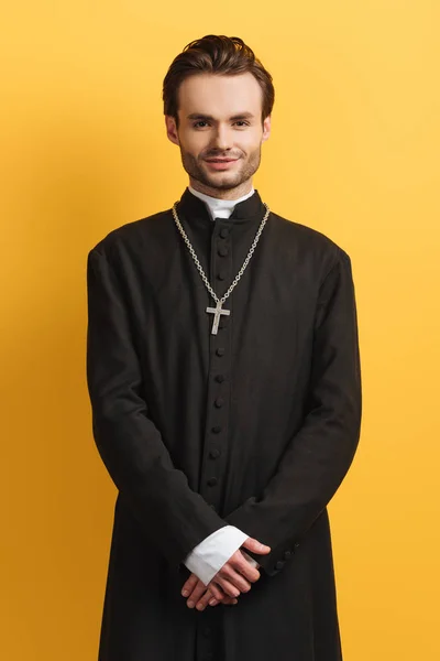 Jeune prêtre catholique souriant à la caméra tout en se tenant isolé sur jaune — Photo de stock