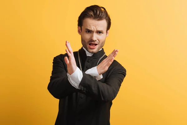 Disgustado sacerdote católico mostrando gesto de stop y mirando a la cámara aislada en amarillo - foto de stock