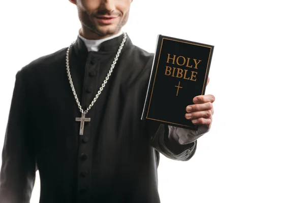 Обрізаний вид на молодого католицького священика, що показує святу Біблію ізольовано на білому — стокове фото