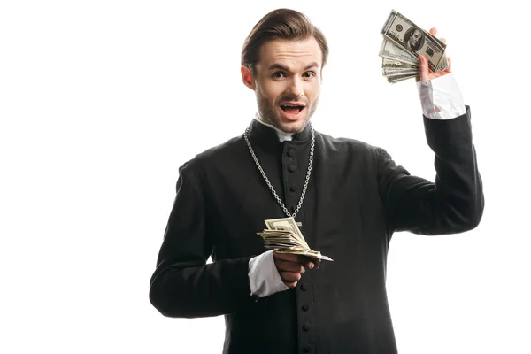 Excited catholic priest looking at camera while showing dollar banknotes isolated on white — Stock Photo