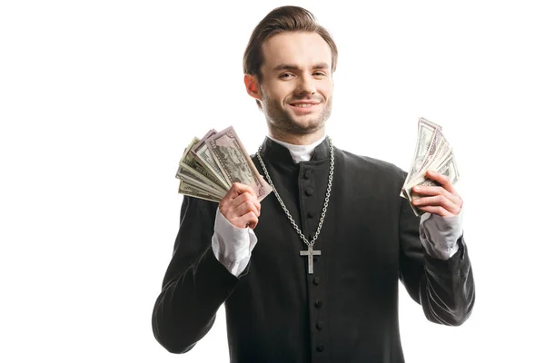 Sacerdote católico corrupto sonriendo a la cámara mientras sostiene billetes de dólar aislados en blanco - foto de stock