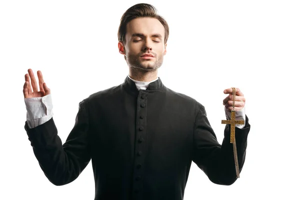 Sacerdote católico concentrado rezando com a mão levantada enquanto segurando a cruz dourada isolada no branco — Fotografia de Stock
