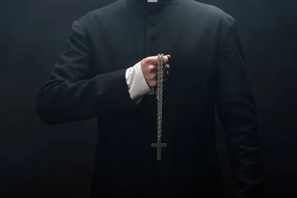 Cropped view of catholic priest holding necklace with silver cross isolated on black — Stock Photo