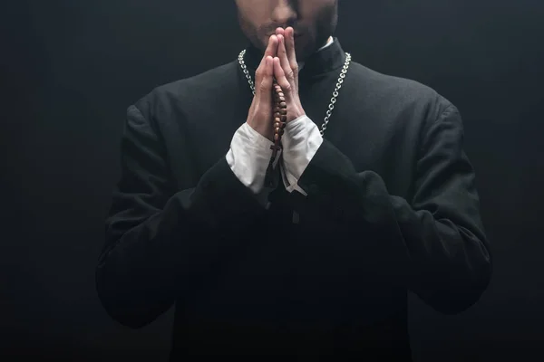 Vista recortada del joven sacerdote católico rezando aislado sobre negro - foto de stock