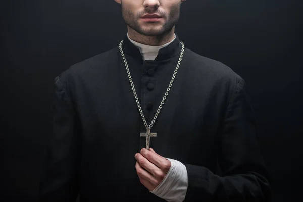 Vue recadrée du prêtre catholique touchant croix d'argent isolé sur noir — Photo de stock