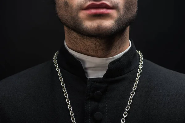Vista recortada del sacerdote católico en sotana negra con collar de plata aislado en negro - foto de stock