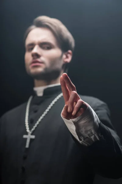 Low angle view of confident catholic priest showing blessing gesture isolated on black — Stock Photo