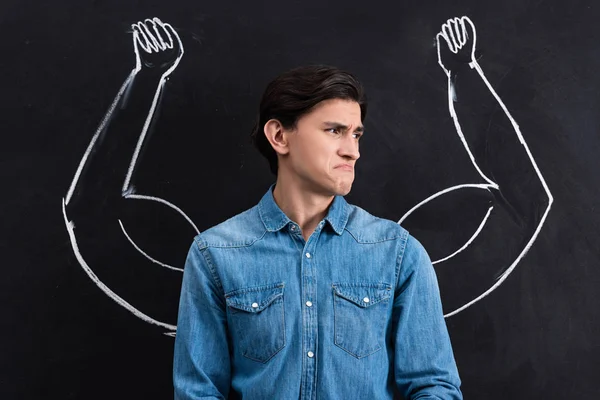 Émotionnel jeune homme avec de forts bras musculaires dessin sur tableau noir — Photo de stock