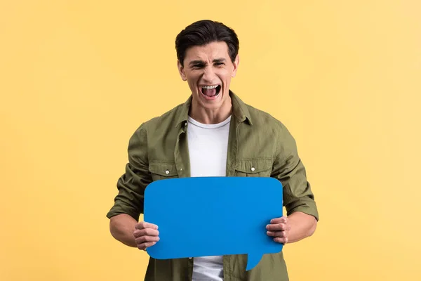 Homem estressado gritando e segurando bolha de fala azul, isolado em amarelo — Fotografia de Stock