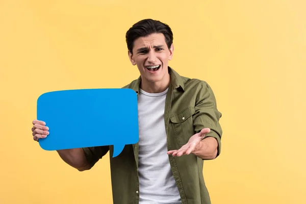 Angry man holding blue speech bubble, isolated on yellow — Stock Photo