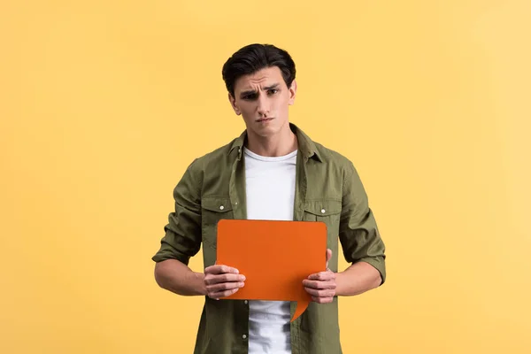 Skeptical man holding orange speech bubble, isolated on yellow — Stock Photo