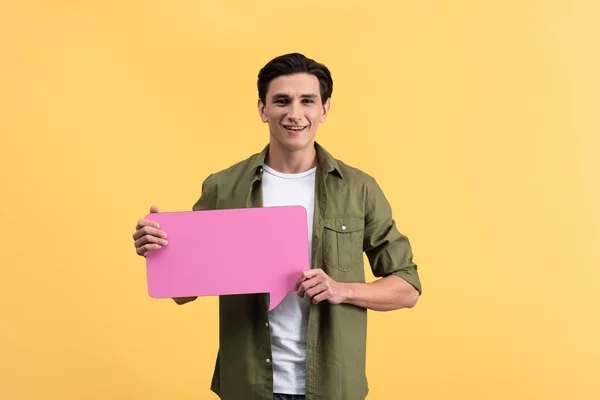 Усміхнений чоловік тримає рожеву бульбашку мовлення, ізольований на жовтому — стокове фото
