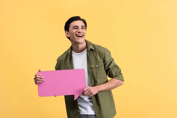 Hombre alegre sosteniendo burbuja de habla rosa, aislado en amarillo - foto de stock