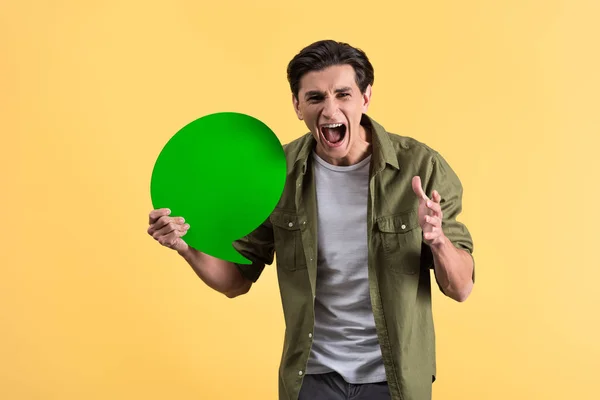 Aggressive man shouting and holding green speech bubble, isolated on yellow — Stock Photo