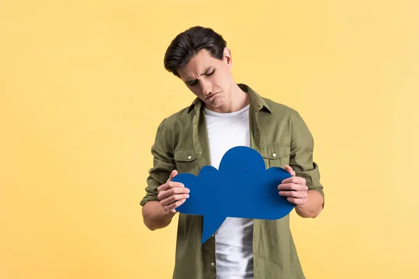 Hombre escéptico sosteniendo burbuja voz nube azul, aislado en amarillo - foto de stock