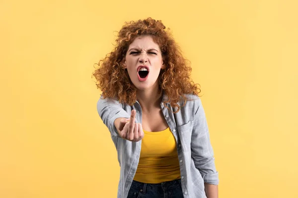 Mulher ruiva agressivo gritando e mostrando dedo médio, isolado em amarelo — Fotografia de Stock