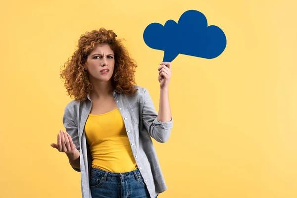 Confused redhead woman holding empty speech bubble in shape of cloud, isolated on yellow — Stock Photo