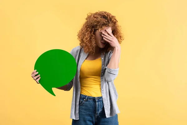 Menina ruiva frustrada segurando bolha discurso verde vazio, isolado no amarelo — Fotografia de Stock