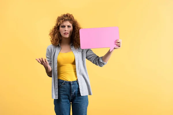 Beautiful confused girl holding empty pink speech bubble, isolated on yellow — Stock Photo