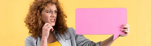 Plano panorámico de chica asustada mirando la burbuja del habla de color rosa vacío, aislado en amarillo - foto de stock