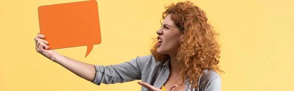 Tiro panorâmico de menina irritada olhando para bolha discurso laranja vazio, isolado no amarelo — Fotografia de Stock